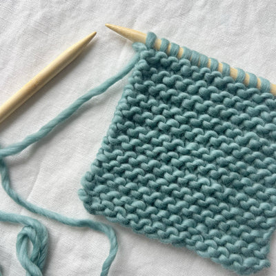 Teal knitted fabric with wooden knitting needles on a light background