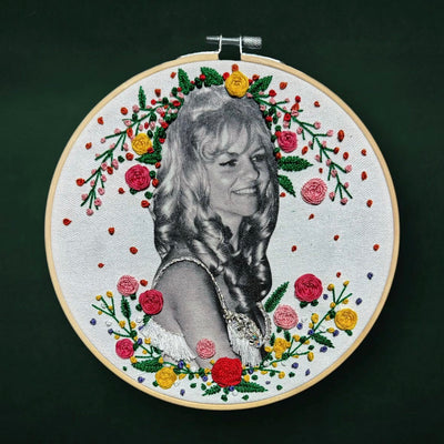 An embroidery hoop displaying a black and white photograph of a woman, adorned with colorful embroidered flowers and leaves.