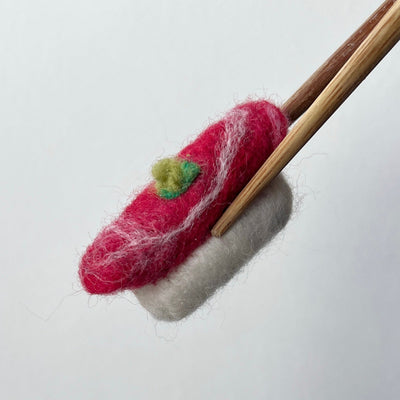 Felted sushi held by wooden chopsticks on a white background