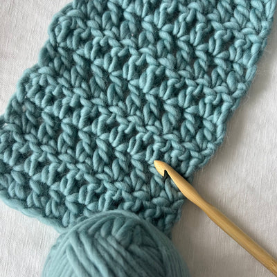 Knitted teal fabric with a wooden crochet hook on a light background