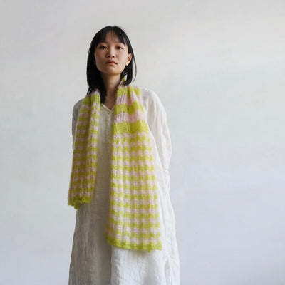Woman wearing a yellow and green checkered scarf against a plain background