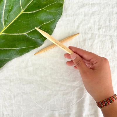 Hand holding a wooden tool with a green leaf on a white fabric background