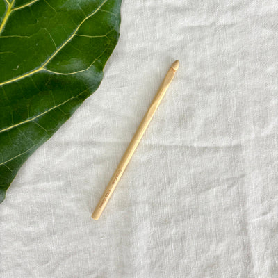 Gold crochet hook on a textured white fabric surface with a green leaf