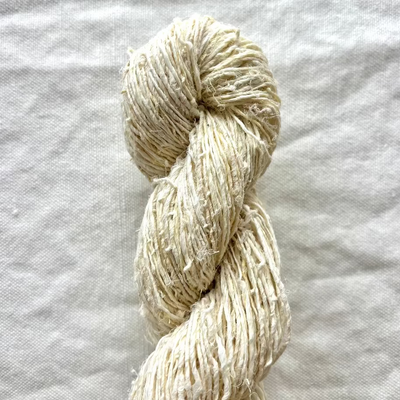 Coiled skein of beige yarn on a textured white fabric background