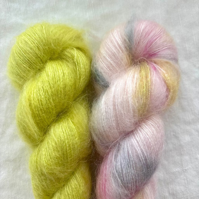 Two skeins of yarn, one green and one pink with yellow tones, on a light gray background.