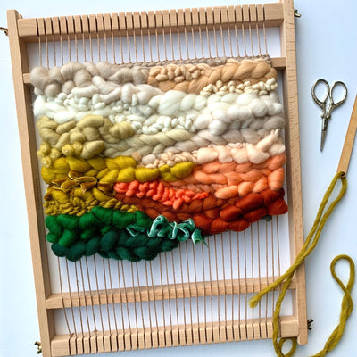 Weaving loom with colorful yarn and tools on a light background