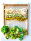 Wool fiber art on a loom with green and white fibers