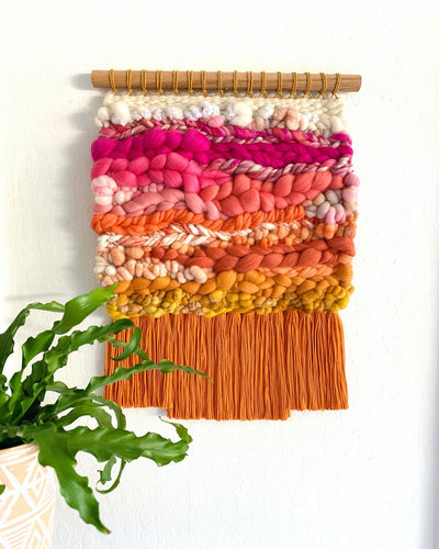 Colorful woven wall art with a plant on a white background