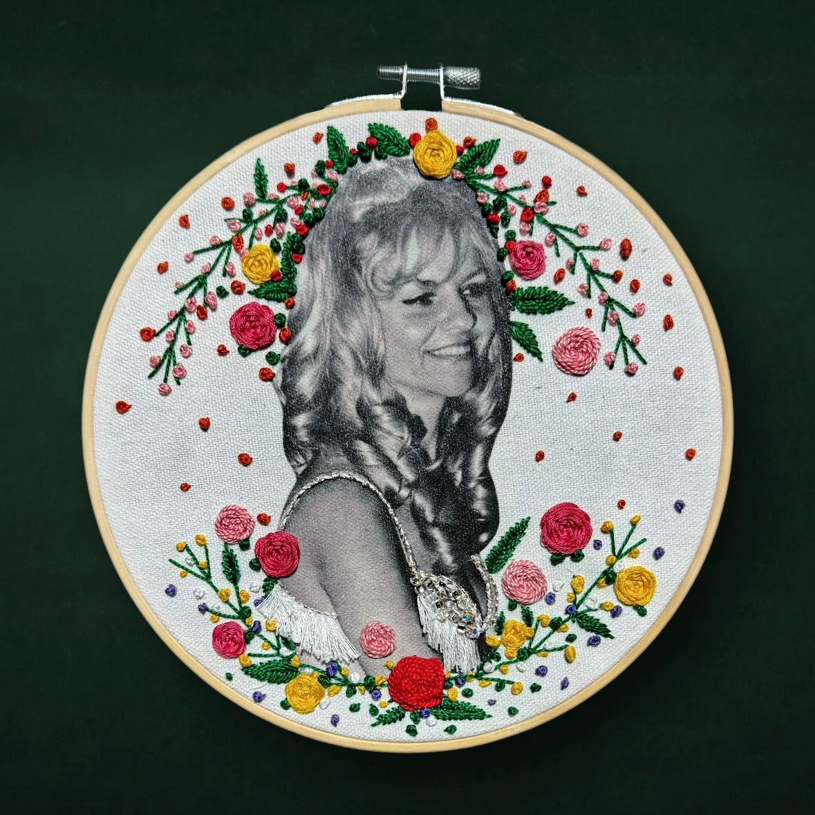 An embroidery hoop displaying a black and white photograph of a woman, adorned with colorful embroidered flowers and leaves.