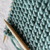 Knitted fabric with teal yarn and wooden knitting needles on a light background