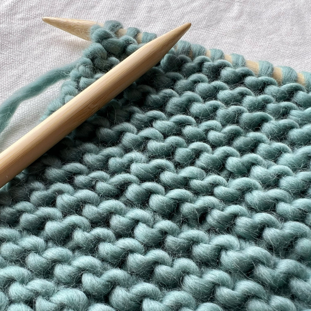 Knitted fabric with teal yarn and wooden knitting needles on a light background