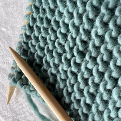 Knitted fabric with teal yarn and wooden knitting needles on a light background