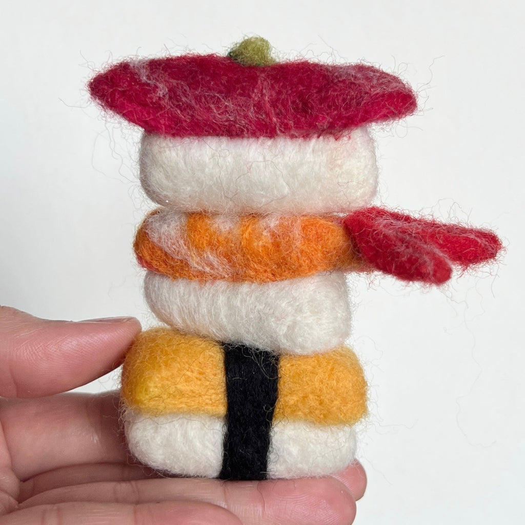 Stack of felted sushi with a hand holding it against a white background