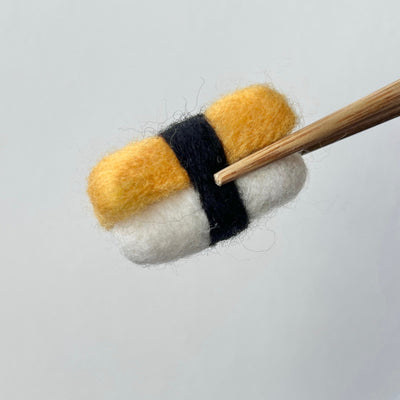 Felt sushi roll with black band and wooden chopsticks on a light gray background