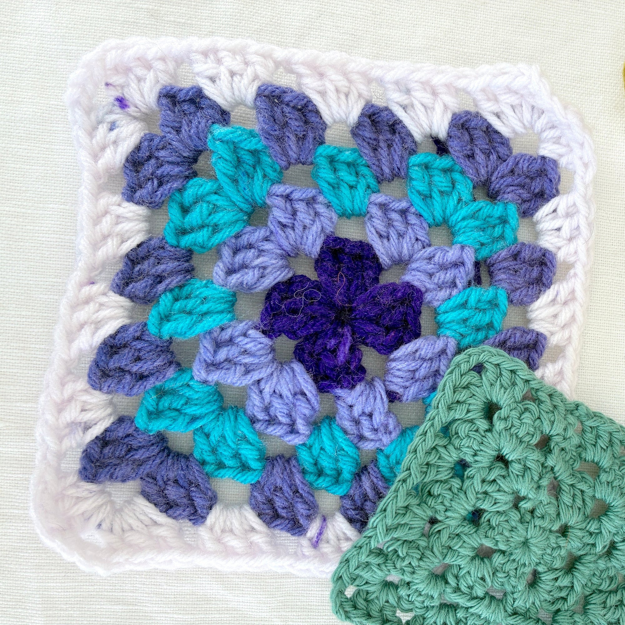 Crocheted square with a wooden crochet hook on a white background