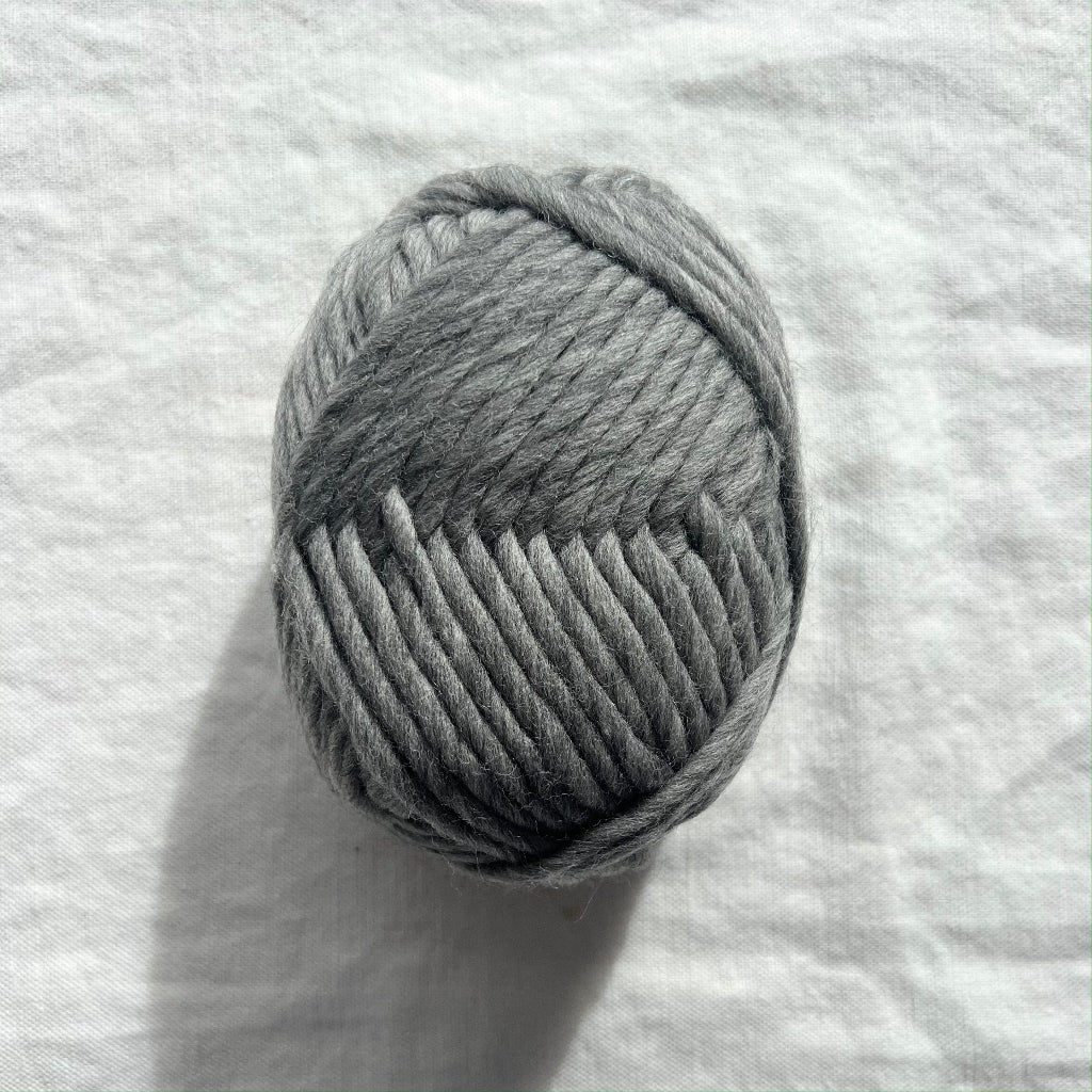 Ball of gray yarn on a white fabric background