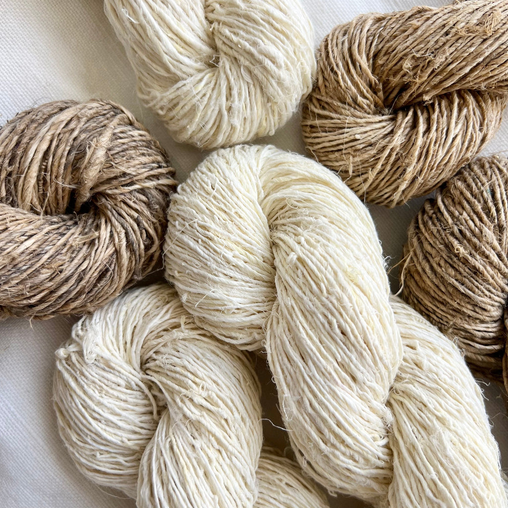 Collection of hemp yarn skeins in beige and white on a light background