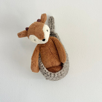 A brown plush deer toy with a white face and small antlers, nestled inside a gray knitted crocheted basket against a plain white wall.