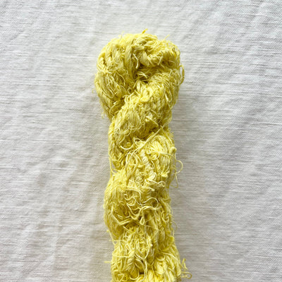 A skein of fluffy, curly yellow yarn laid vertically on a textured off-white linen background.