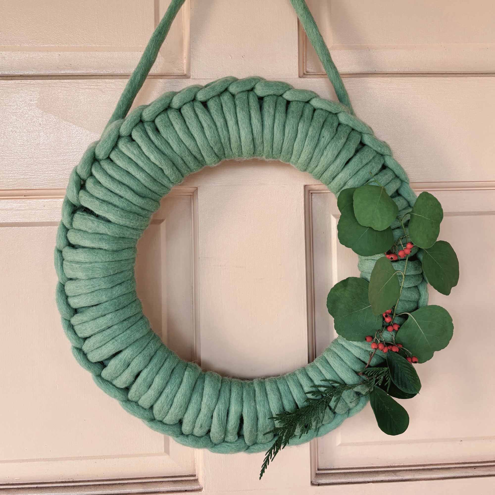 Felted wool wreath in green yarn on a pink door