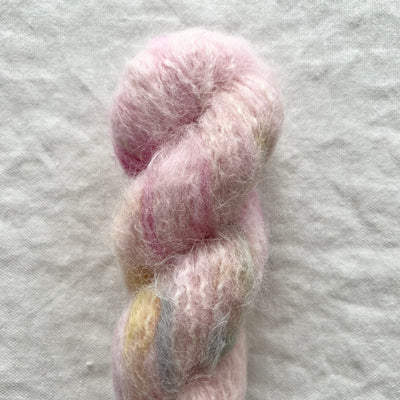 Pastel pink and yellow yarn skein on a textured light gray background