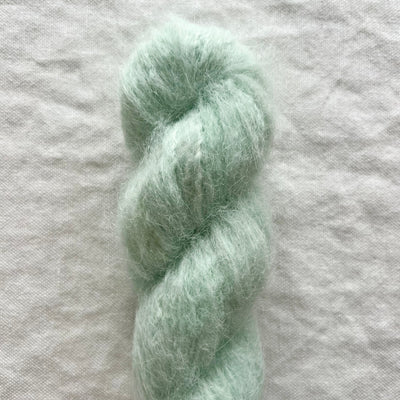 Mint green skein of yarn on a light gray fabric background