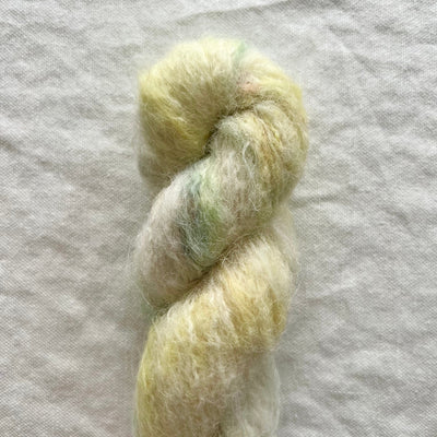 Skein of light yellow and green yarn on a white fabric background