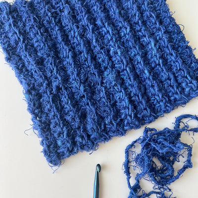 Blue textured knitted fabric with a crochet hook on a light background