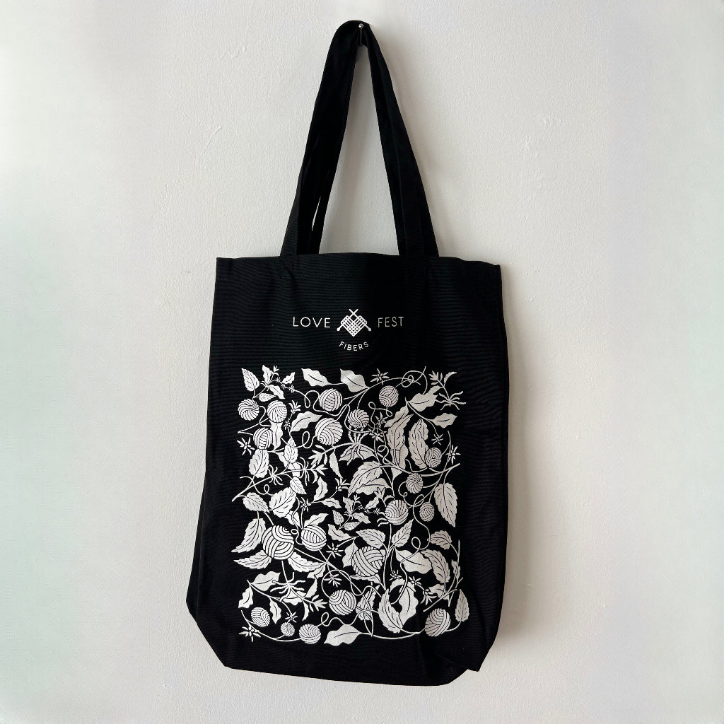 Black tote bag with white floral design and text on a light gray background
