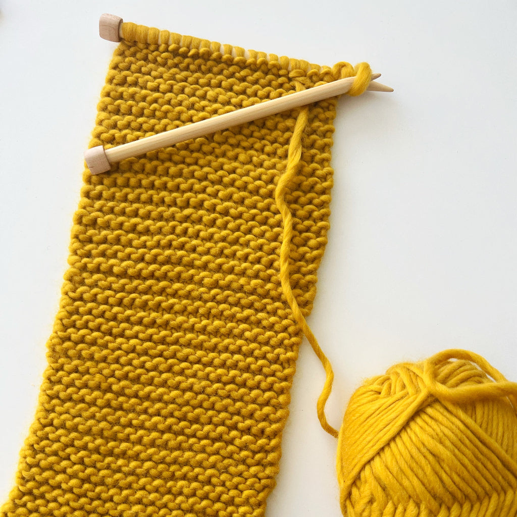 knitting needles with yellow yarn scarf in process