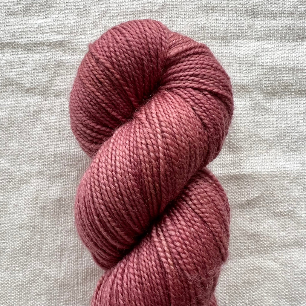 Mauve skein of yarn on a light gray fabric background