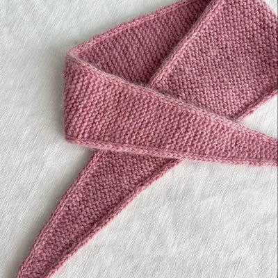 Pink knitted scarf on a light wooden surface