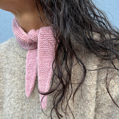 Close-up of a pink knitted scarf around a person's neck with a blurred background