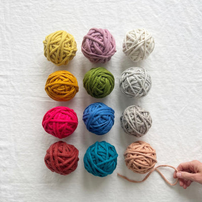 Assorted colorful yarn balls on a textured white surface with a hand holding yarn.