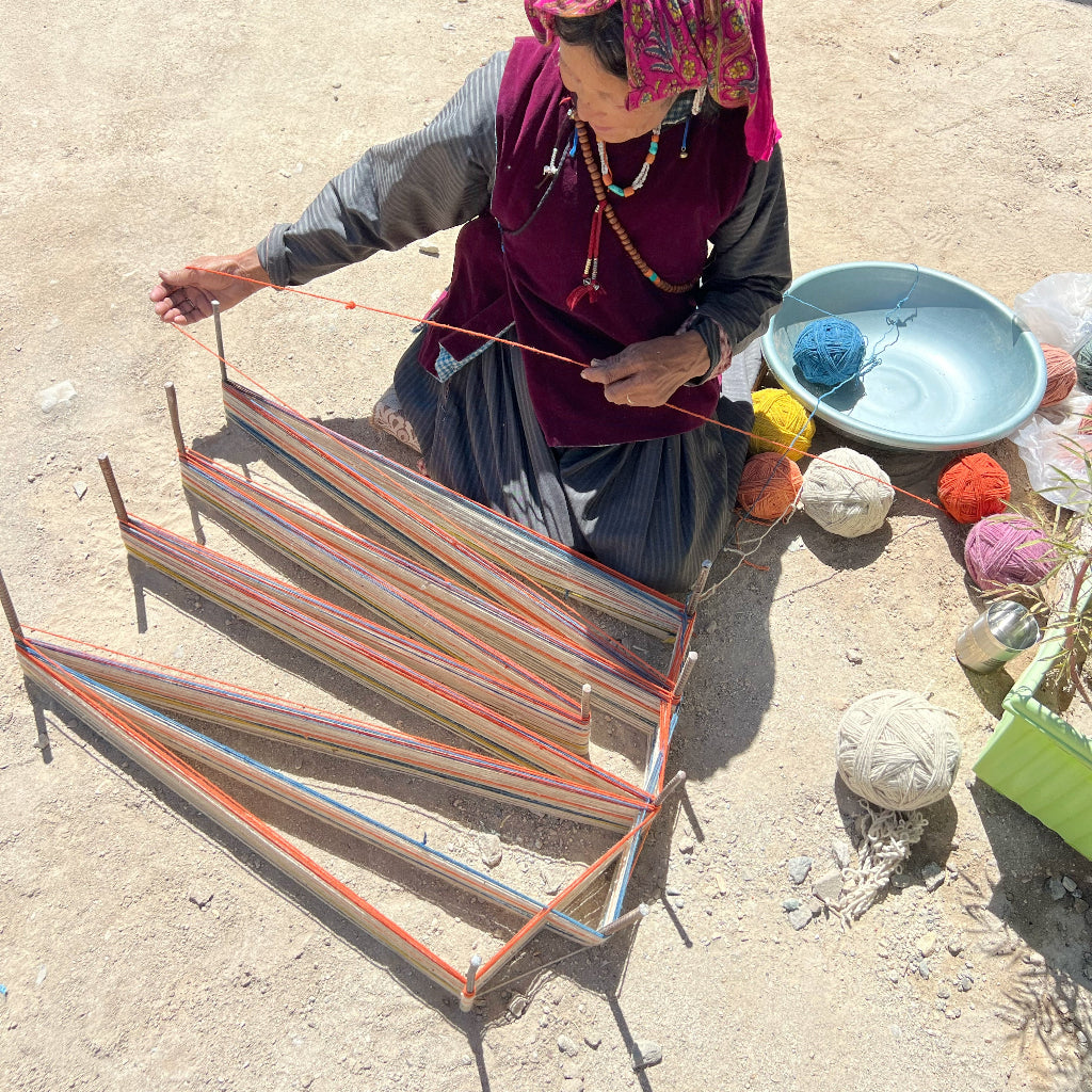 Woman weaving with colorful yarn on a sandy surface