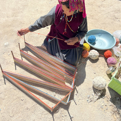 Woman weaving with colorful yarn on a sandy surface