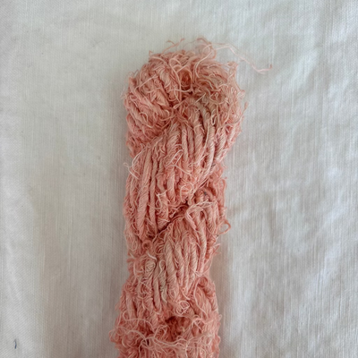 Pink textured yarn skein on a light beige fabric background