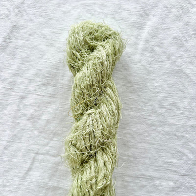 A skein of light green yarn laid vertically on a textured white fabric background