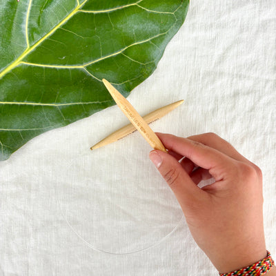 Hand holding wooden knitting needles with a green leaf on a white fabric background