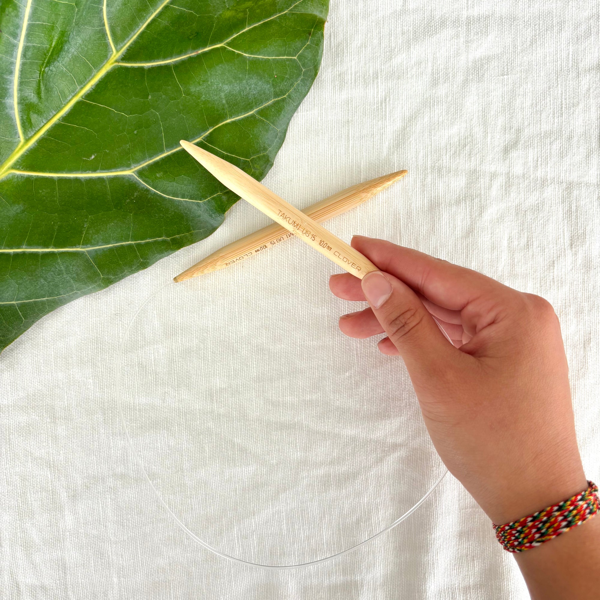 Hand holding a wooden tool with a green leaf on a white fabric background