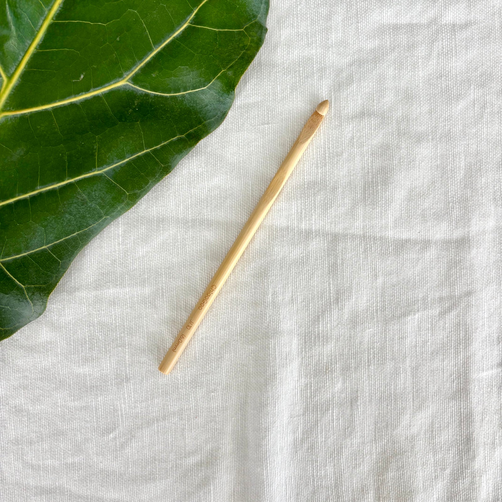 crochet hook on a textured white fabric surface with a green leaf