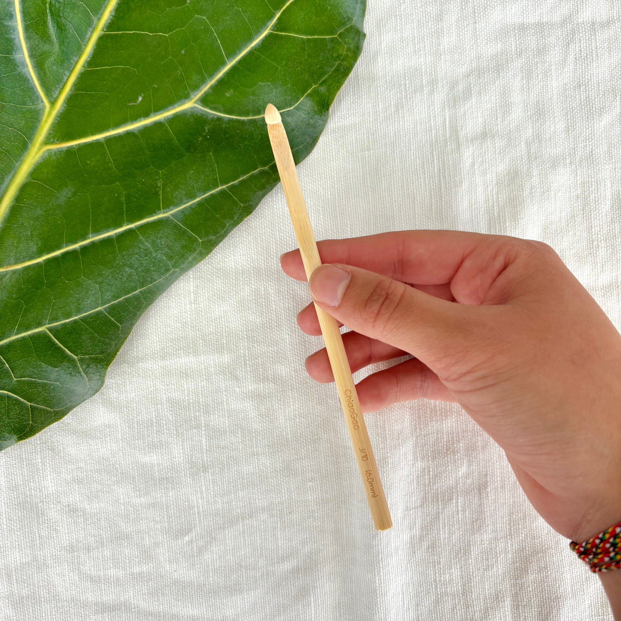 Hand holding a wooden stick next to a green leaf on a white fabric background