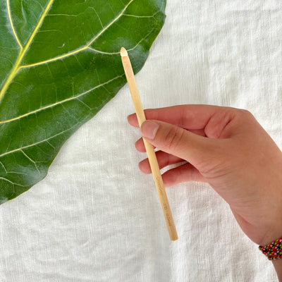 Hand holding a wooden stick next to a green leaf on a white fabric background