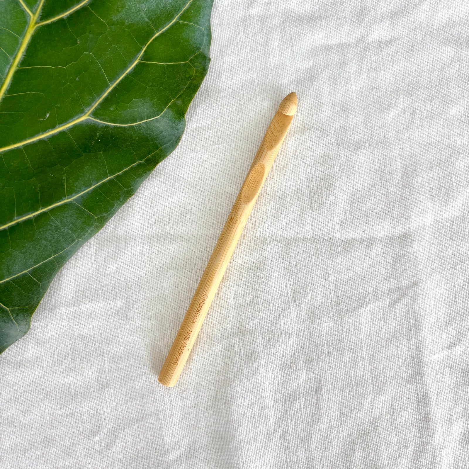 Wooden crochet hook on a textured white fabric surface with a green leaf.