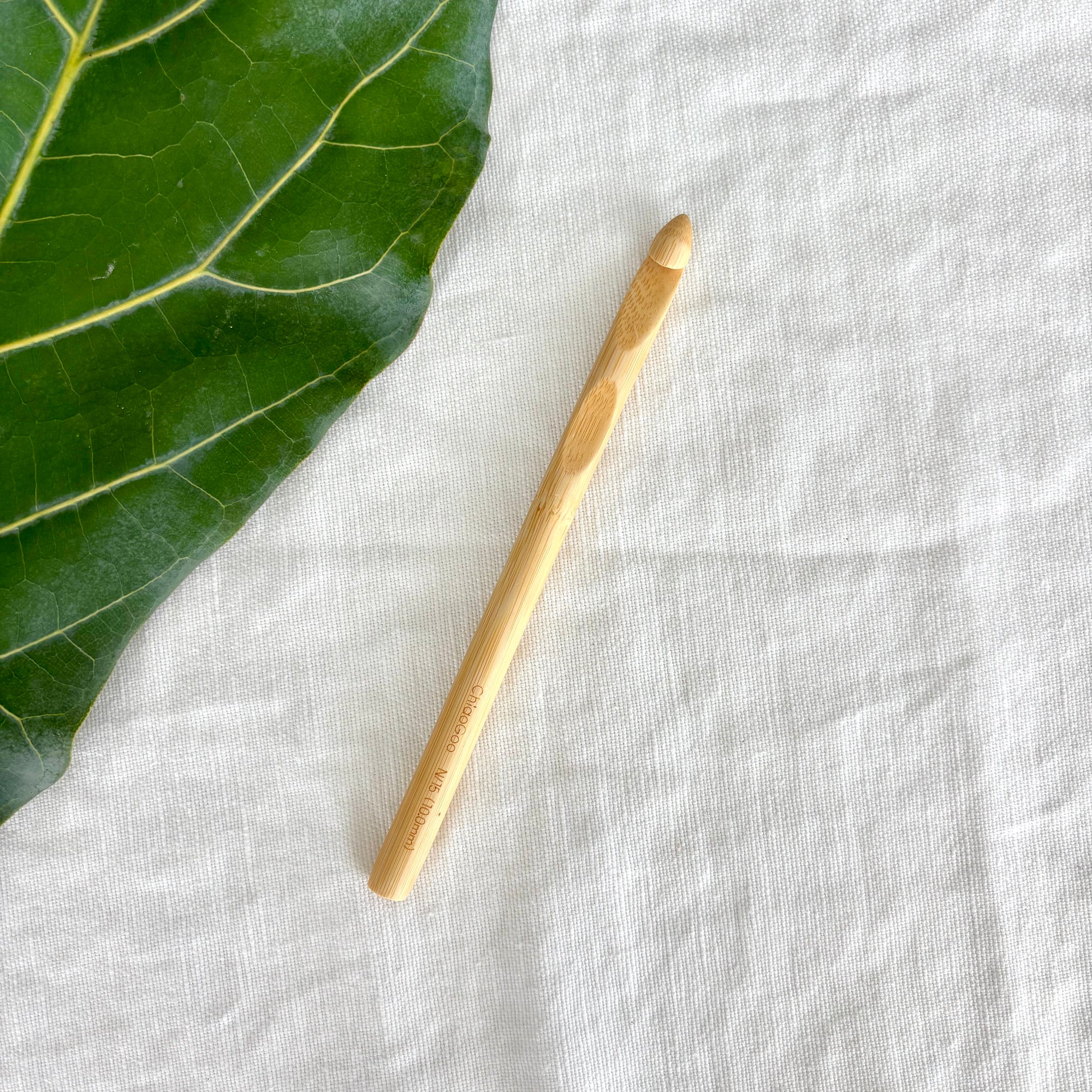 Wooden crochet hook on a textured white fabric surface with a green leaf.