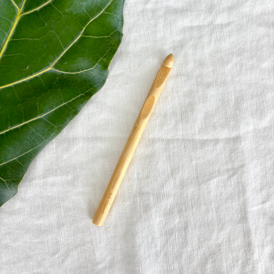 Wooden crochet hook on a textured white fabric surface with a green leaf.