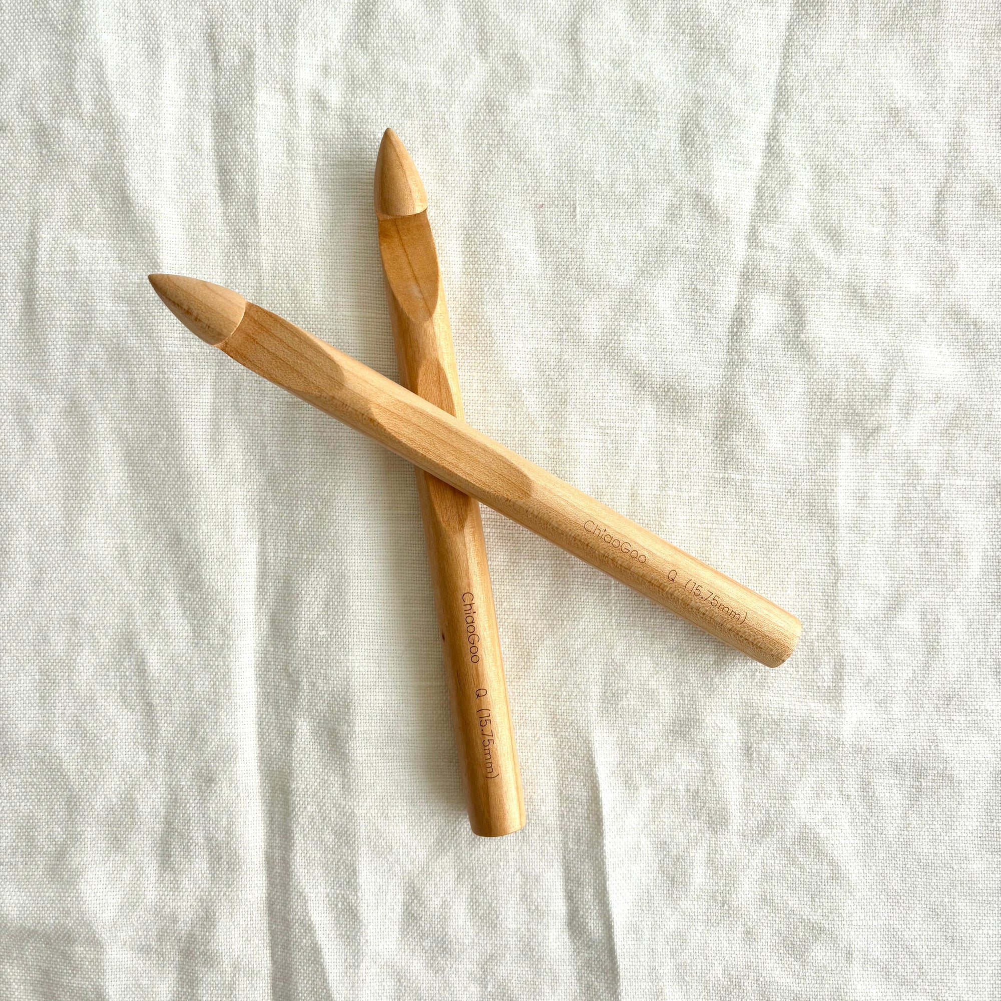 Two wooden crochet hooks on a textured white fabric background