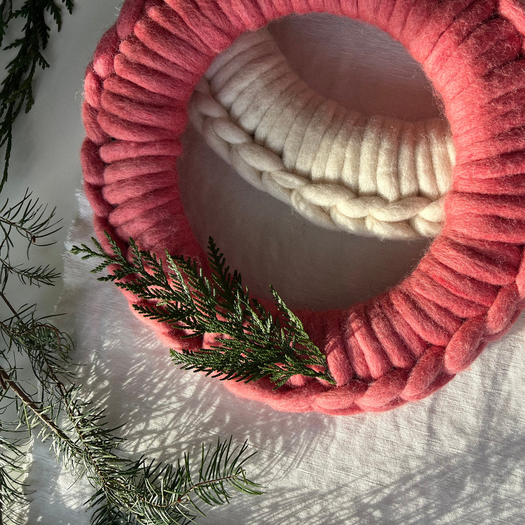 Pink and white textured yarn wreath with a wooden crochet hook on a light background