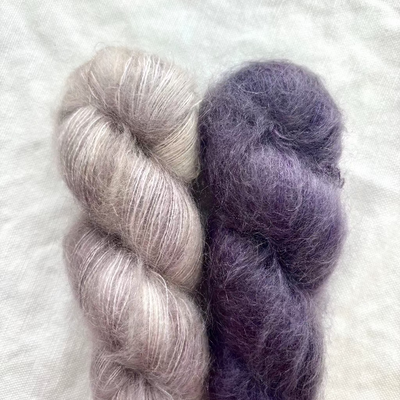 Two skeins of yarn, one purple and one gray, on a textured white background.