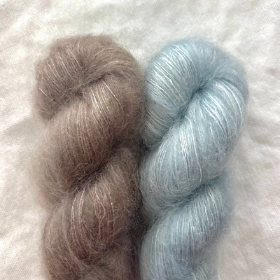 Two skeins of yarn, one brown and one light blue, on a textured white background.